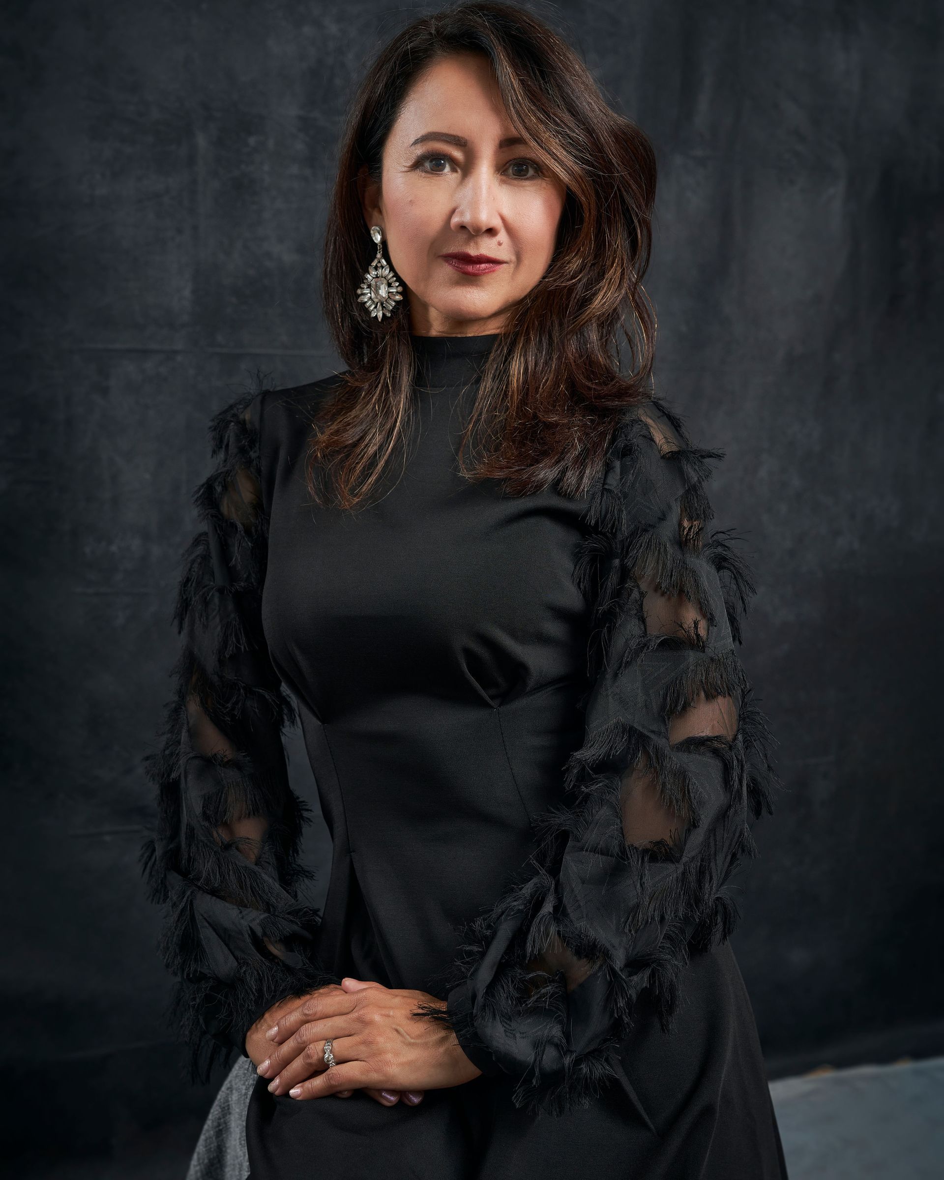 A woman in a black dress is standing in front of a black background.