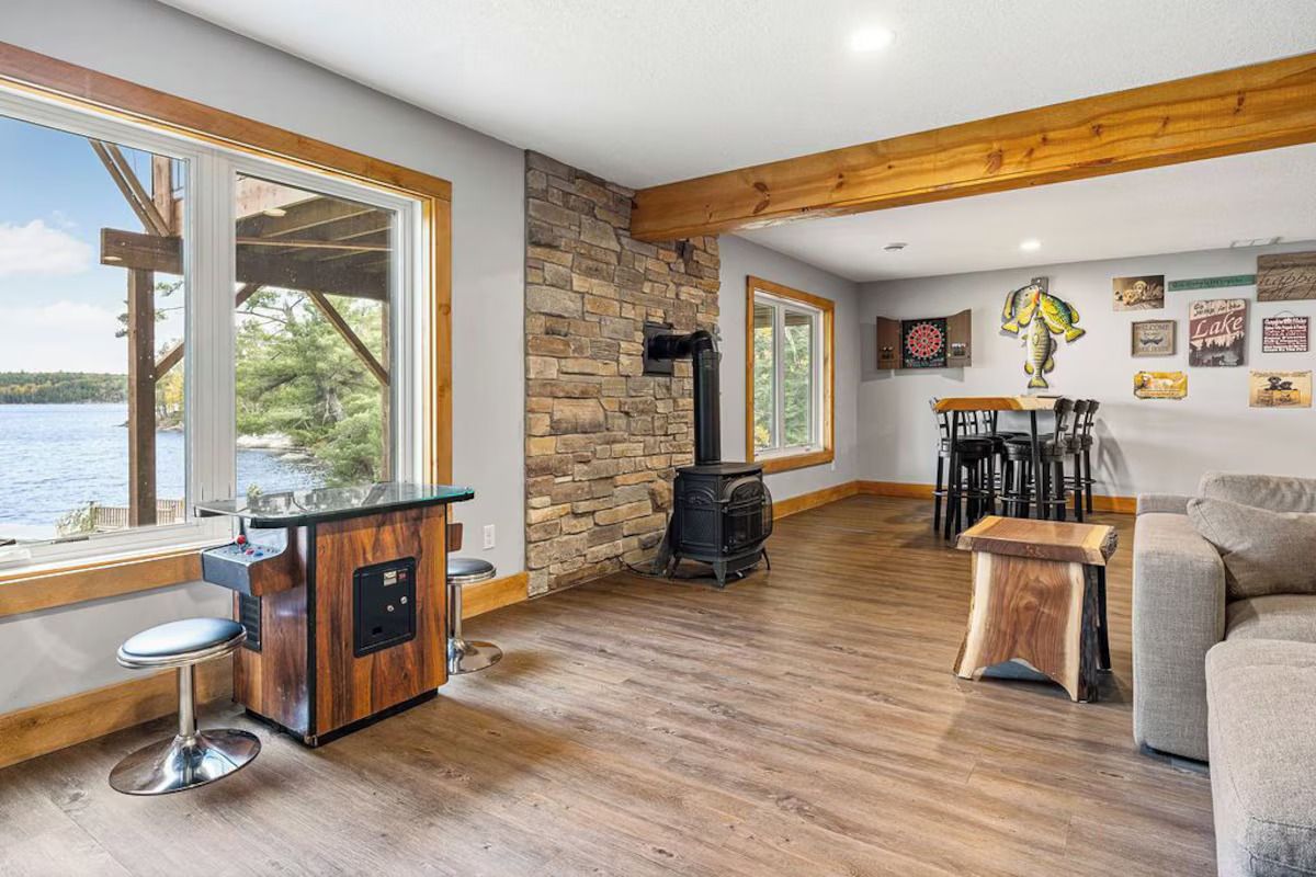Room with lake view, stone wall, wood stove, arcade game, and seating.