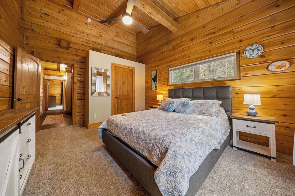 Bedroom with log walls, bed with floral bedding, nightstand, and window.