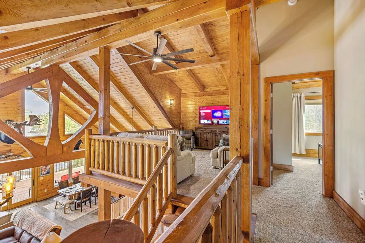 Wooden cabin interior with a loft, overlooking a dining area and a living room with a TV.