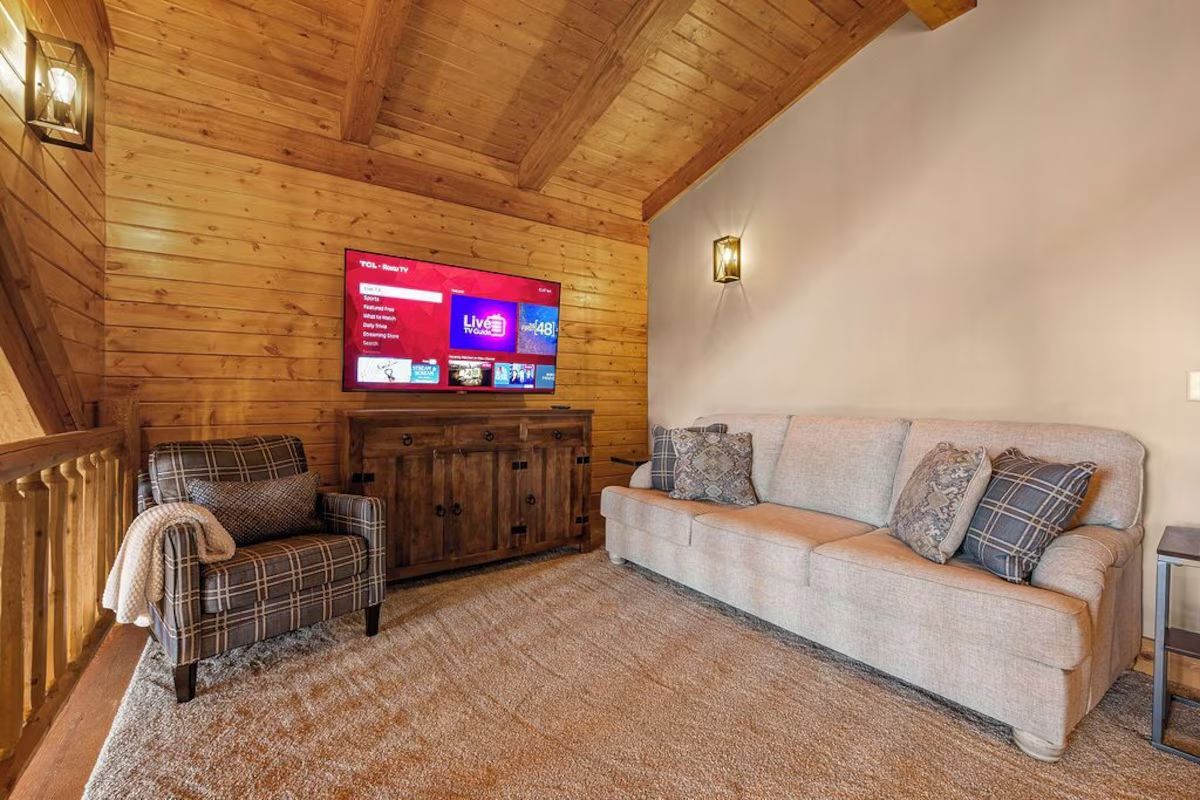A cozy living space with a sofa, armchair, TV, and wooden paneling.