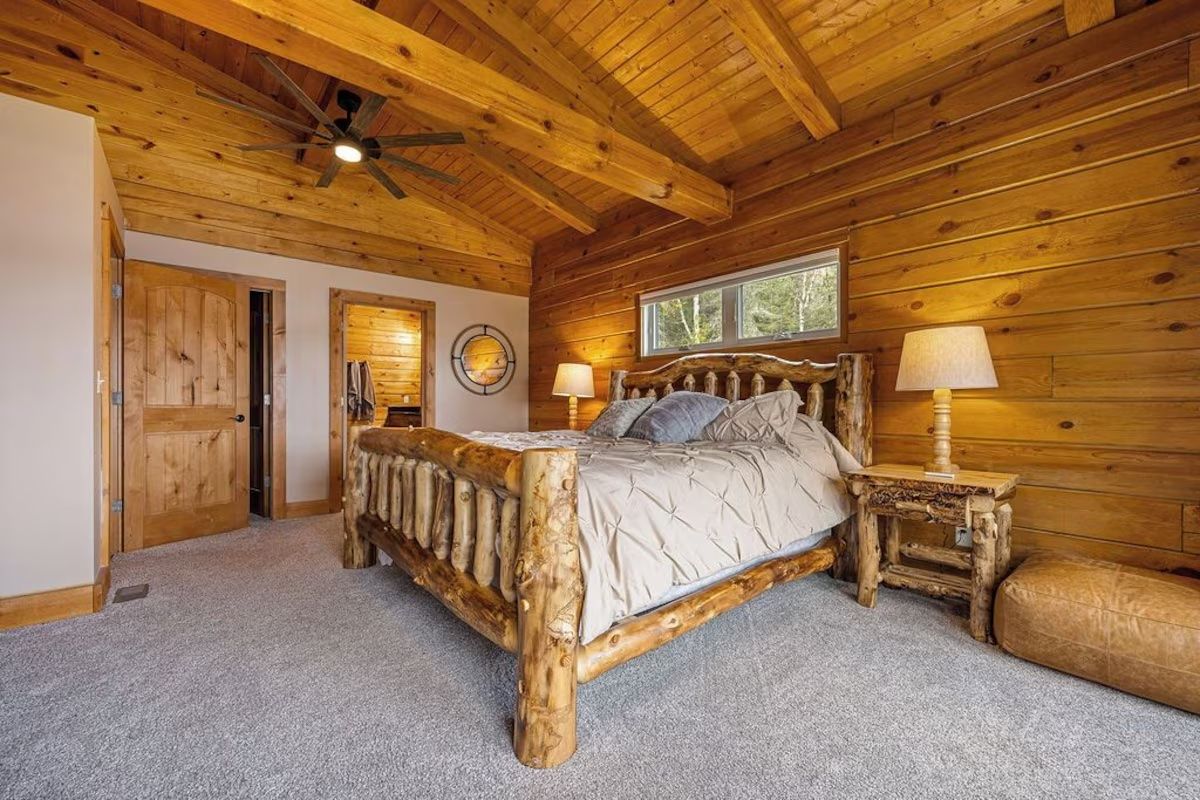 Bedroom with wooden log bed, walls, and ceiling, with bedside lamps and a window.
