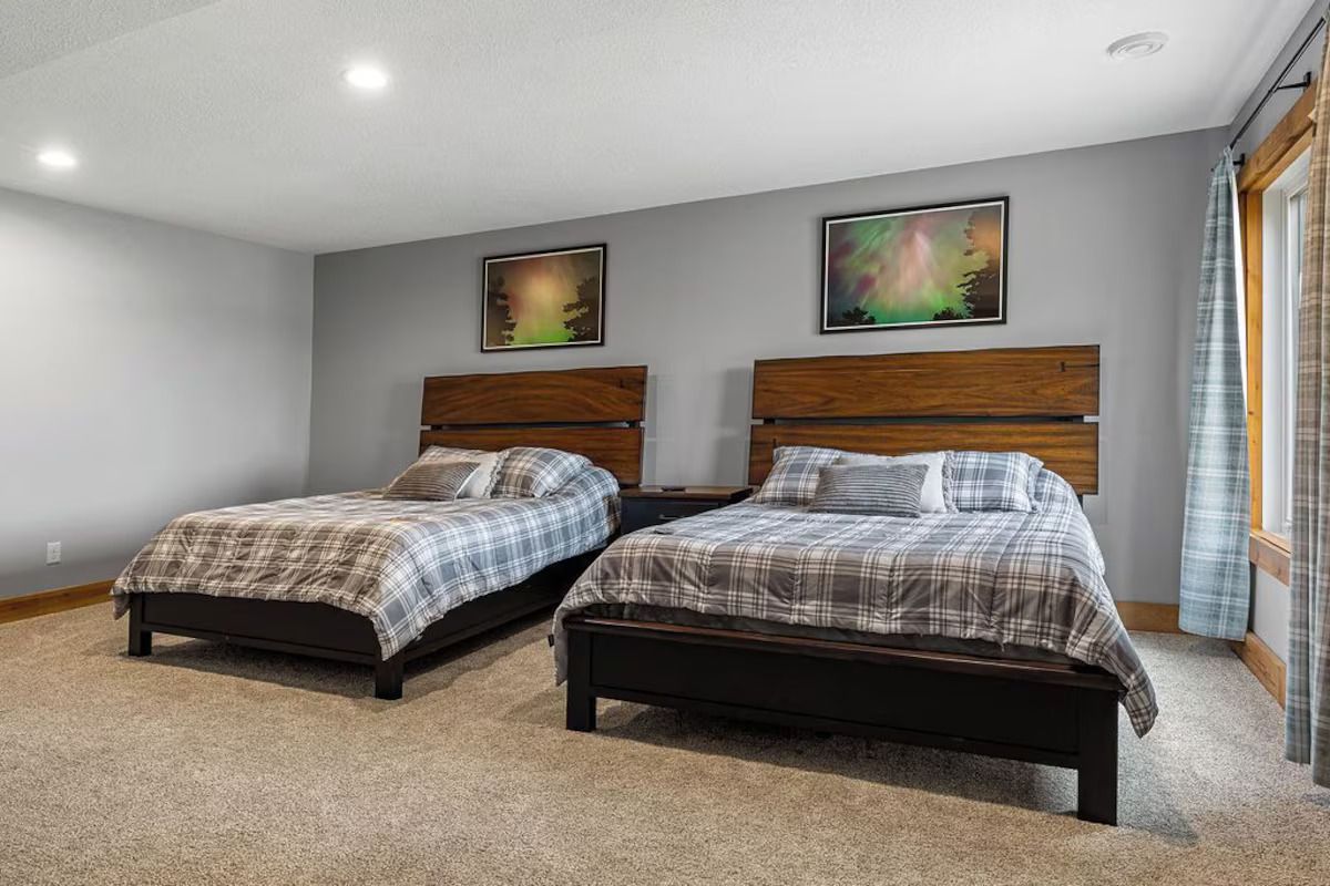 Two twin beds in a room with gray walls, artwork, and a window with a blue curtain.