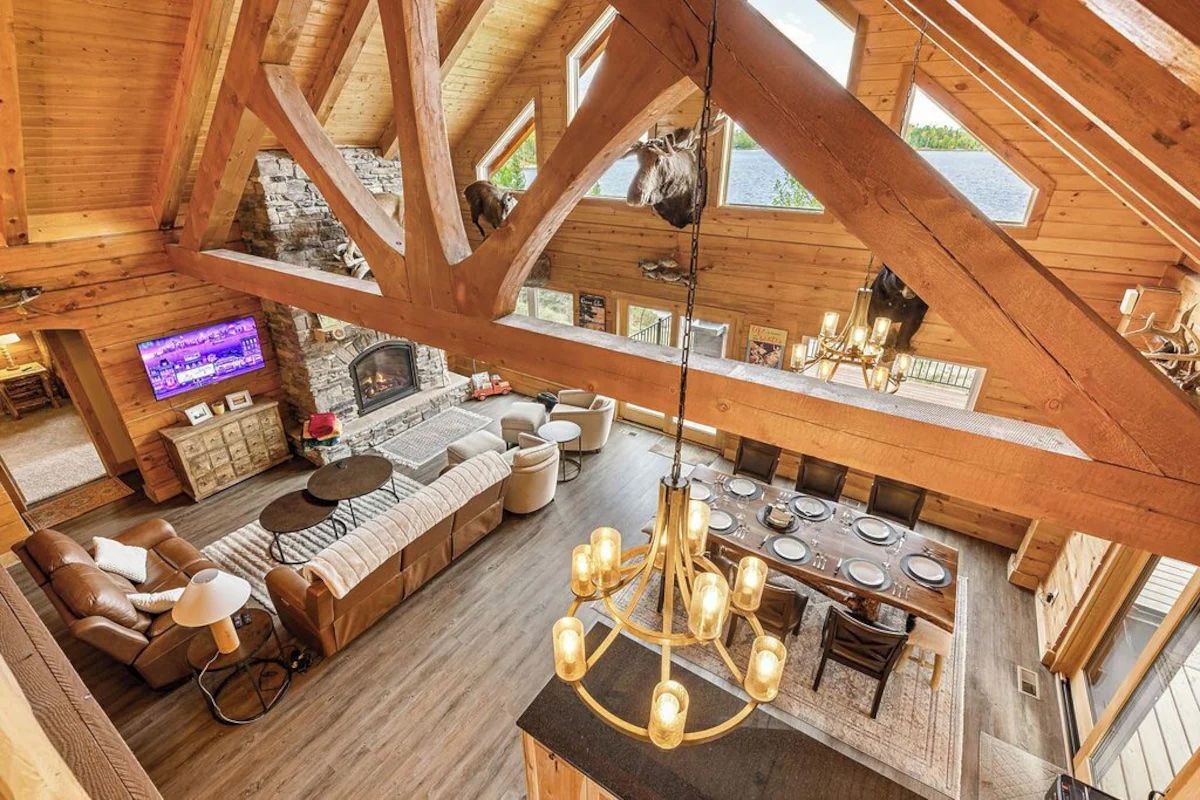 High-angle view of a luxurious log cabin's interior, featuring living room, dining area, and exposed wooden beams.