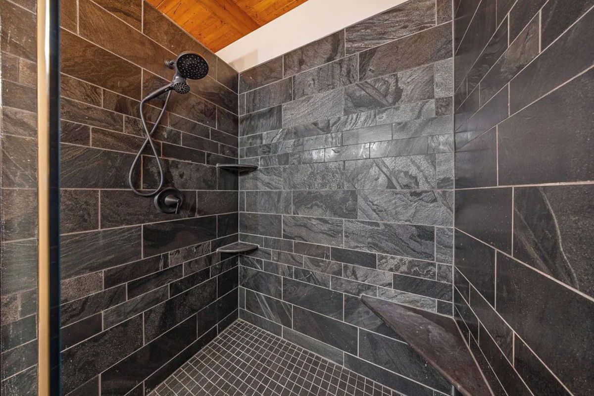 Dark tiled shower with showerhead, shelves, and wood ceiling.