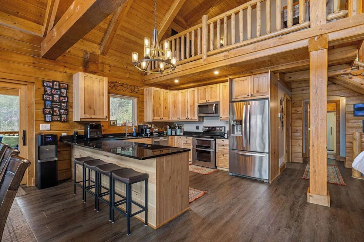 Wooden cabin kitchen with island, stainless steel appliances, and loft overlooking the space.