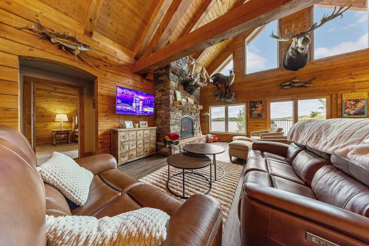 Cozy cabin living room with leather sofas, stone fireplace, and mounted deer and fish.