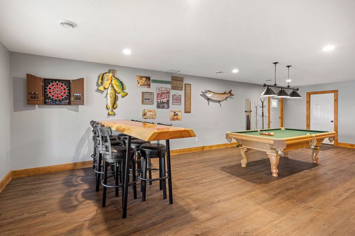 Game room with pool table, bar seating, and dartboard on a wood floor.