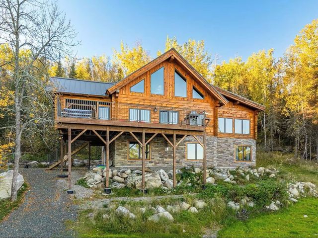 Log cabin style house with stone base and large windows surrounded by trees.