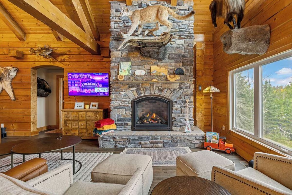 Cozy cabin living room with stone fireplace, wooden beams, and taxidermy.