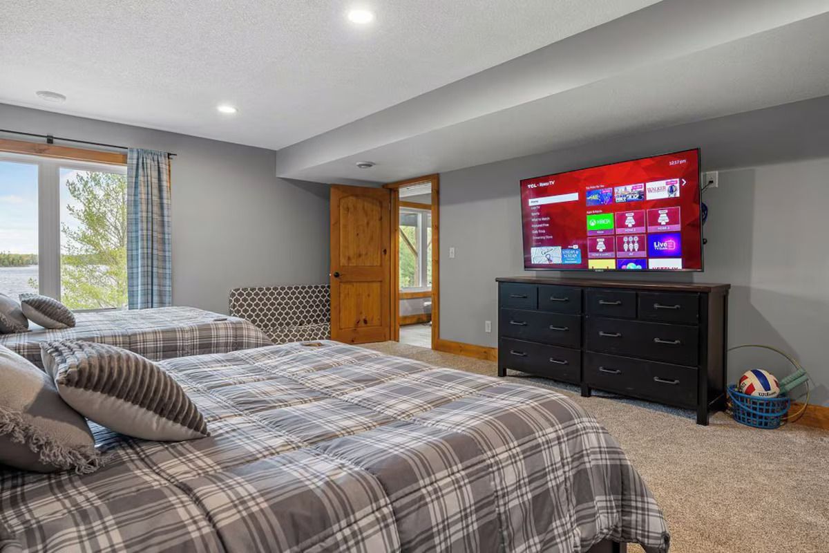 Two beds in a room with a TV, door and window, all with neutral colors.