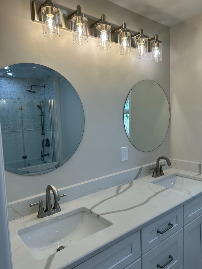 Bathroom with double sinks, round mirrors, and vanity lights over a white countertop.