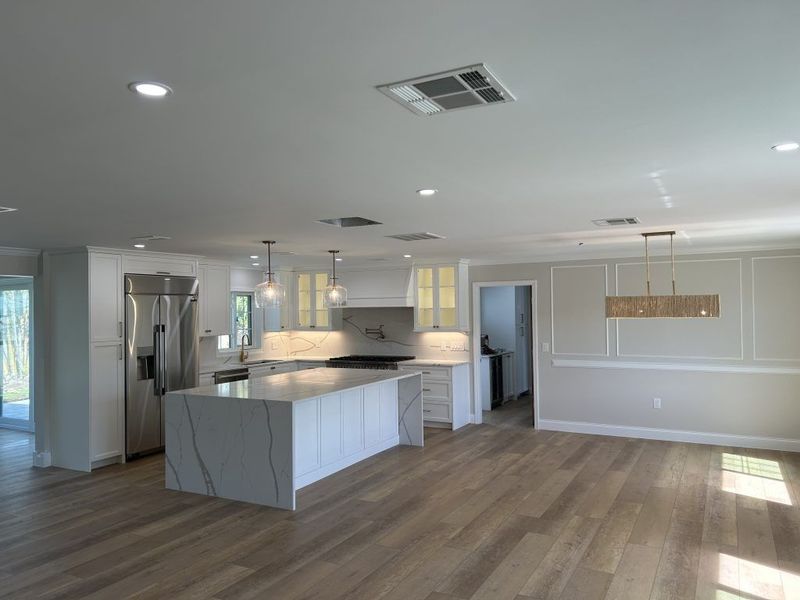 Modern kitchen with white cabinets, island, and stainless steel appliances; light wood floors.