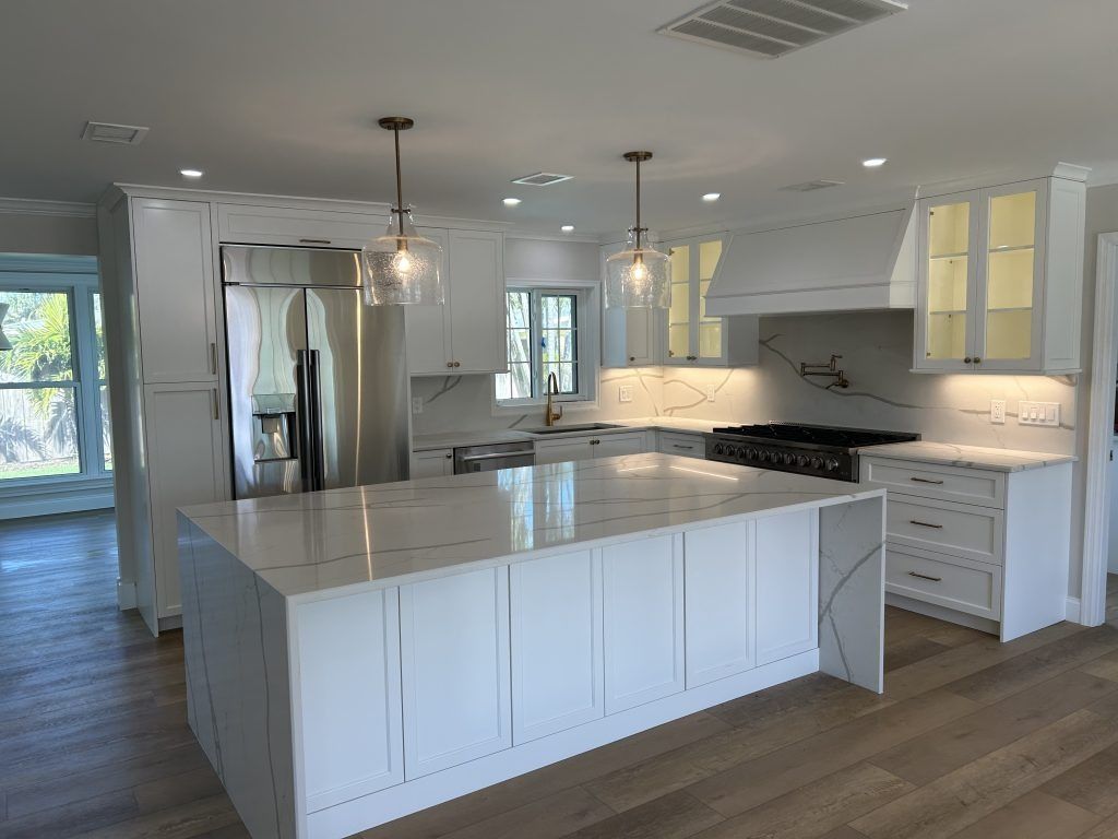 Modern white kitchen with island, stainless steel refrigerator, and pendant lights.