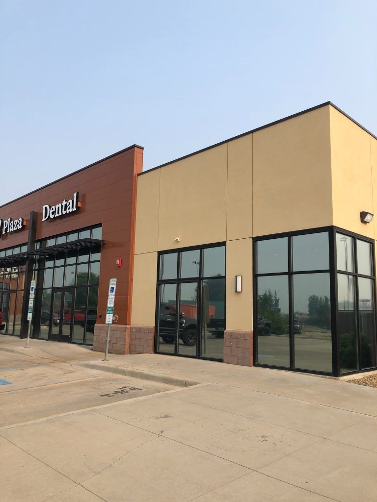 Exterior of a dental office and adjacent building with large windows and tan/brown walls.