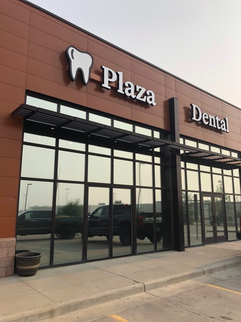 Plaza Dental office exterior with large windows, brown facade, and awning.
