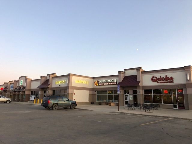 Strip mall with several businesses, including a grocery store, a restaurant, and a Qdoba. Cars are parked.