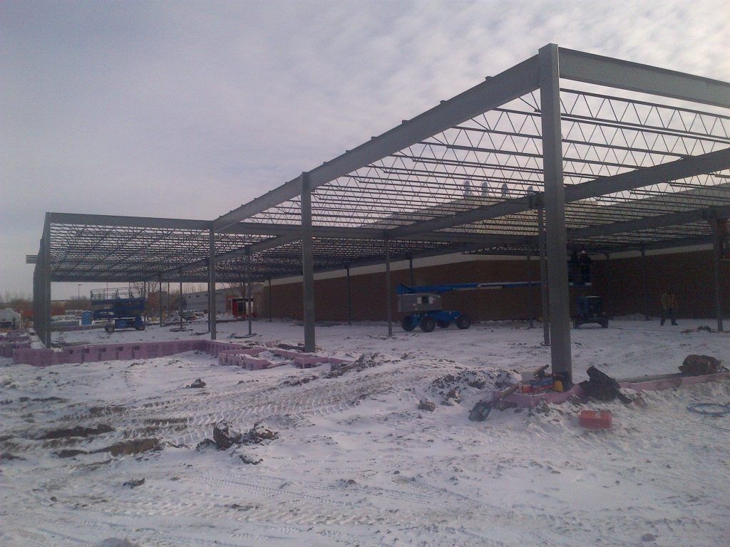 Steel framework of a building under construction, set in a snowy, overcast outdoor environment.