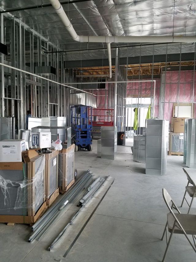 Construction site interior: metal framing, ductwork, materials, and a lift machine.