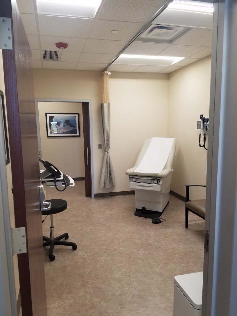 Doctor's office exam room with examination table, chair, and curtained doorway.