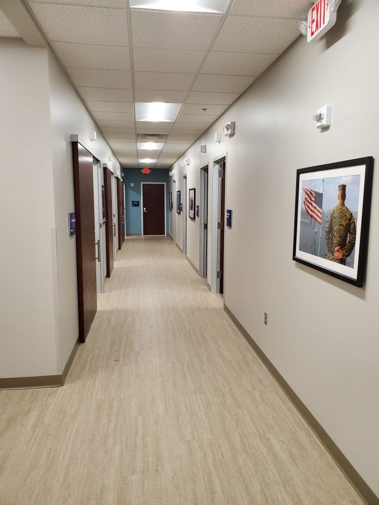 Hallway with closed doors, beige flooring, and a framed photo. An exit sign is visible.