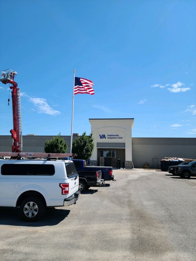 A building with American flag, work trucks parked, and a bright blue sky.