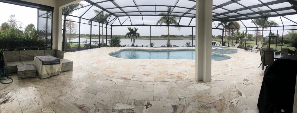 Covered outdoor pool area with patio furniture, stone flooring, and a view of water and trees.