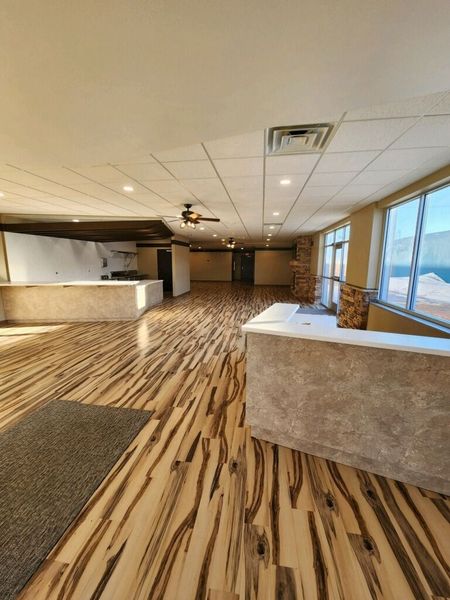 Empty event space with stone-like counters, wood-look flooring, and large windows.