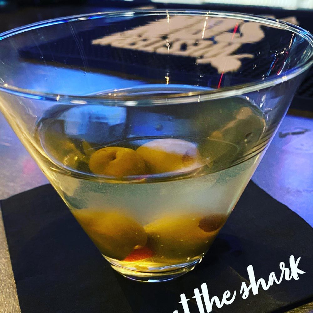 Cocktail in a martini glass with olives on a bar, lit by blue-purple ambient light
