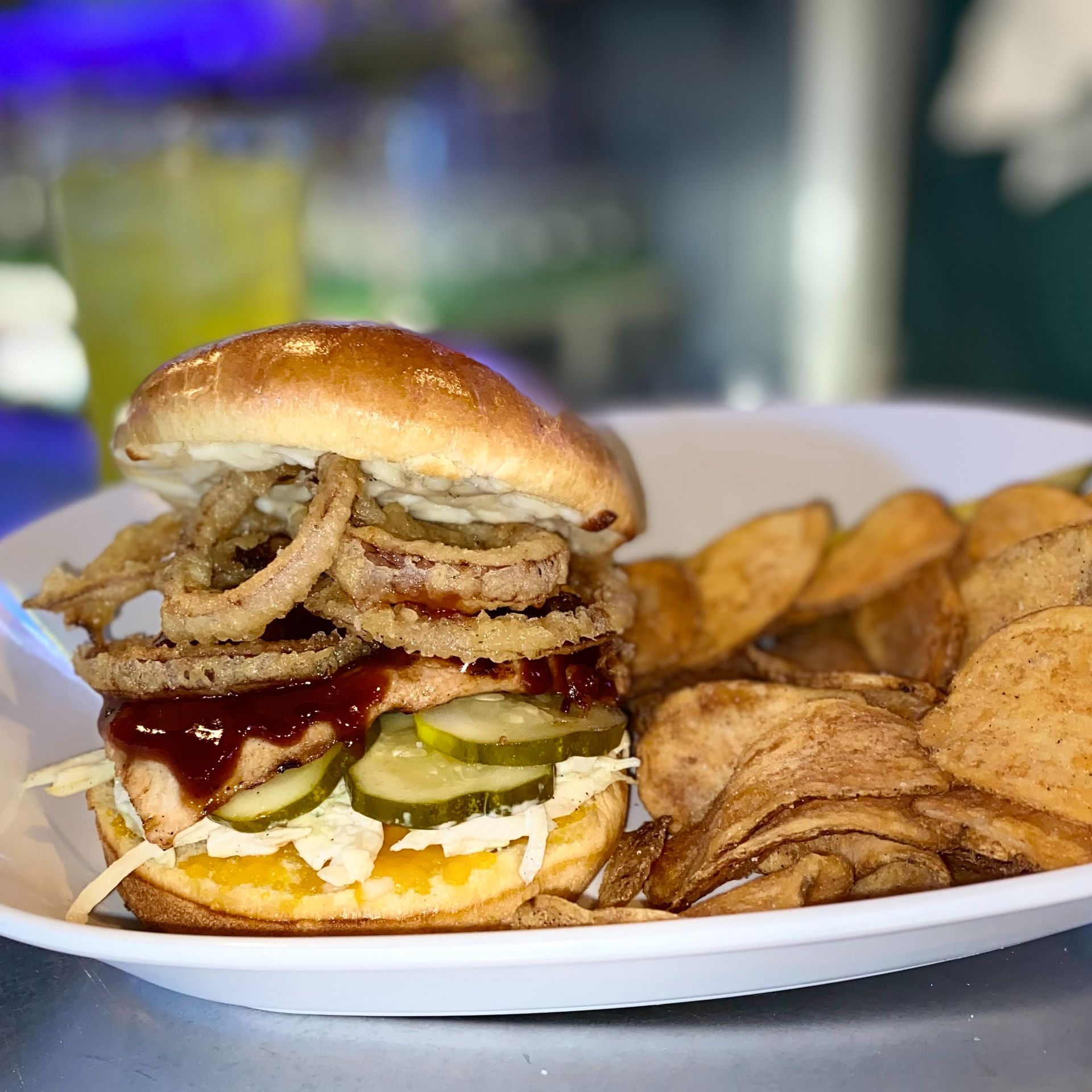 Burger with onion rings, pickles, and fries on a white plate on a table