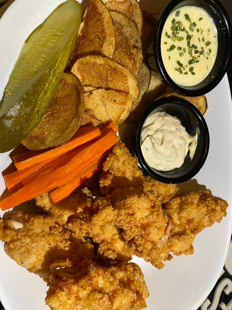 Fried chicken with carrot sticks, pickle slices, fries, and two dipping sauces on a plate