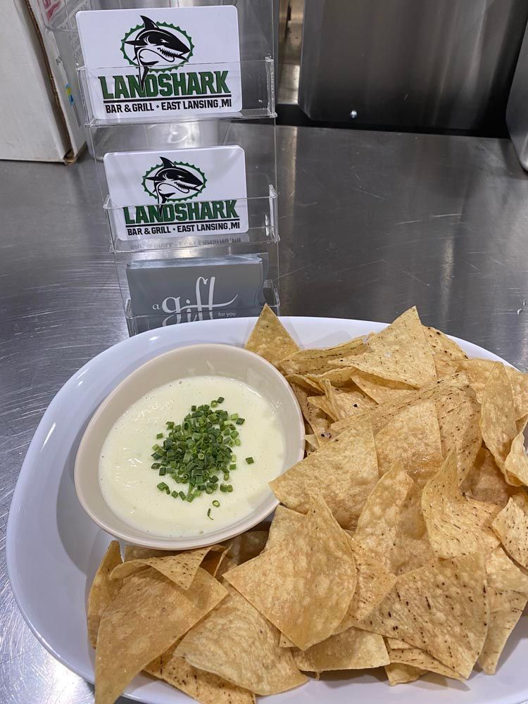 Tortilla chips with queso dip in a bowl on a table, with LandShark branded signs in the background