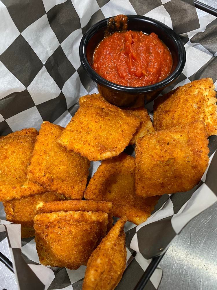 Golden fried bites with a small cup of red dipping sauce in a basket lined with checkered paper