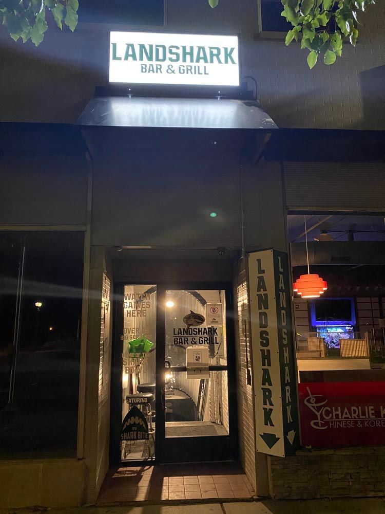 Nighttime storefront of Landshark Bar & Grill with lit sign and glass entrance.