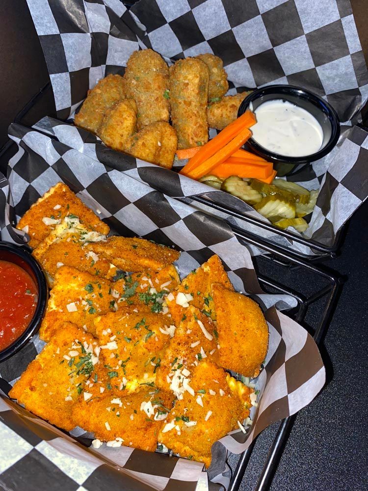 Buffalo chicken tenders with carrot sticks, celery, and dipping sauces in a checkered basket