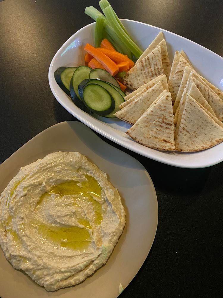 Hummus plate with olive oil beside pita triangles and sliced cucumbers, carrots, and celery sticks