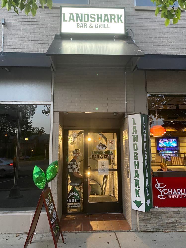 Landshark Bar & Grill entrance with lit sign, green surfboard decor, and indoor TV glow