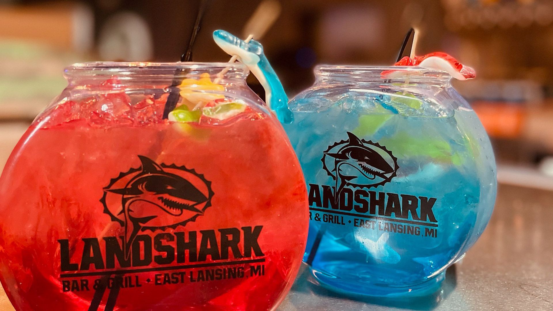 Two colorful fishbowl cocktails, red and blue, with LANOSHARK logos on a countertop.