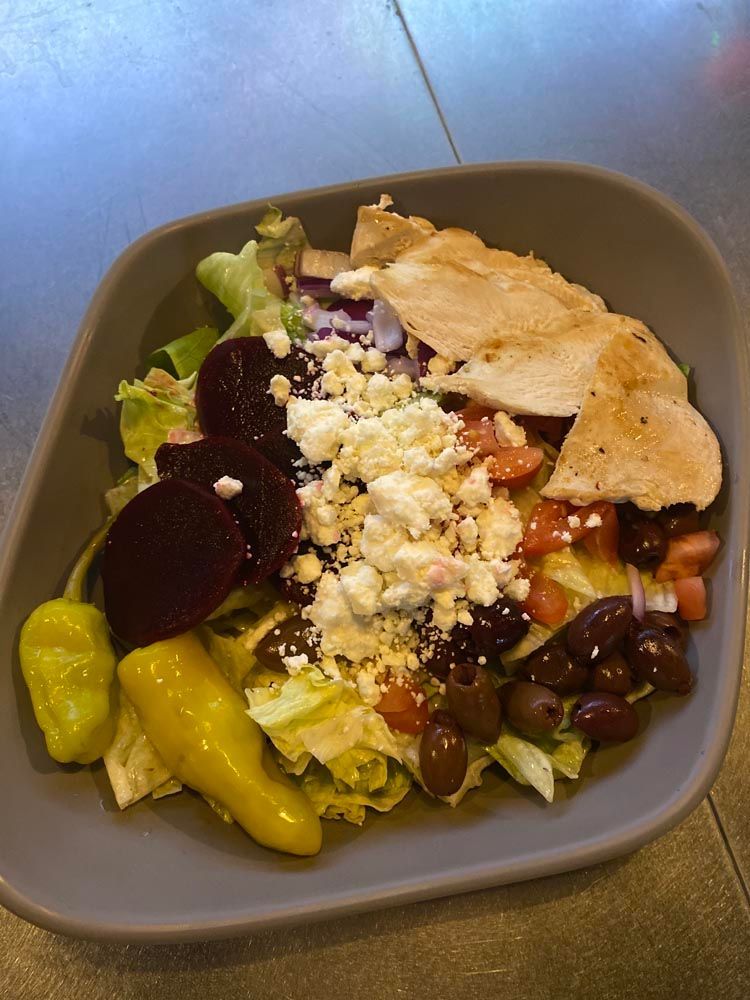 Salad bowl with lettuce, beets, cheese, olives, banana peppers, beans, and grilled chicken on a table