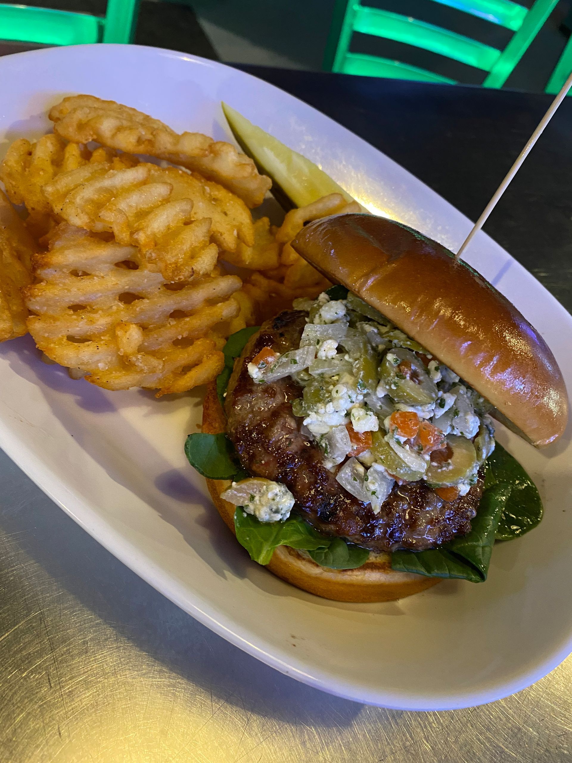 Burger and crinkle-cut fries on a white plate with a pickle spear.