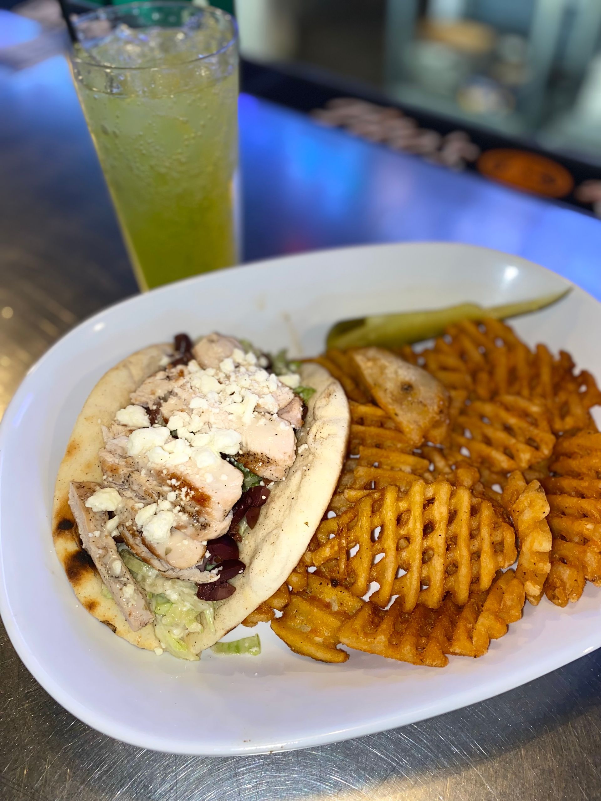 Sandwich and waffle fries on a white plate with a green drink in the background