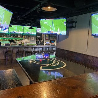 Sports bar interior with multiple TVs showing football over a polished table and empty stools