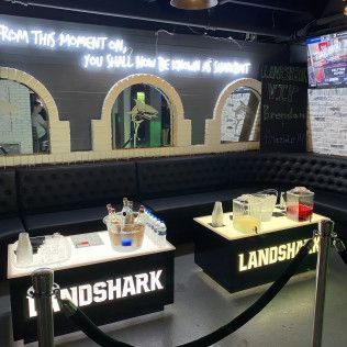 Landshark bar booth with illuminated signs and drinks on tables in a dim indoor venue