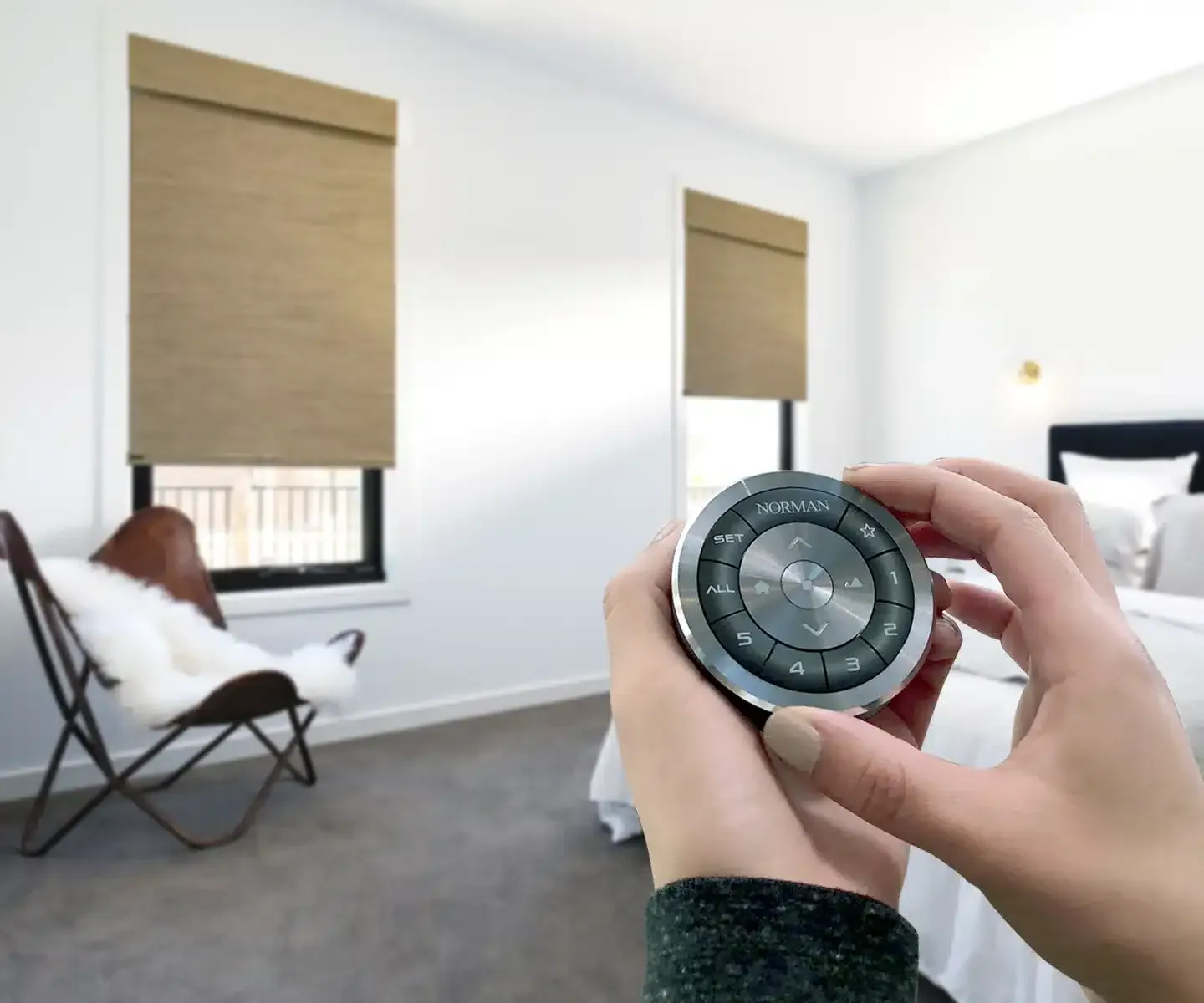 A person holds a circular remote control to operate motorized window shades in a bright, modern bedroom.