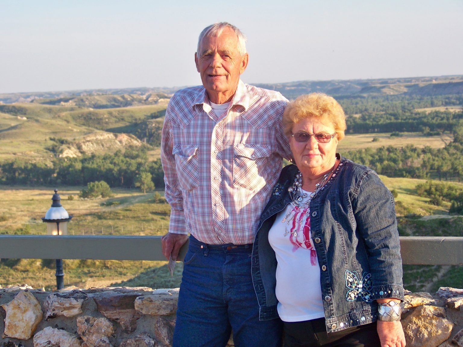 A man and a woman are posing for a picture in front of a landscape.