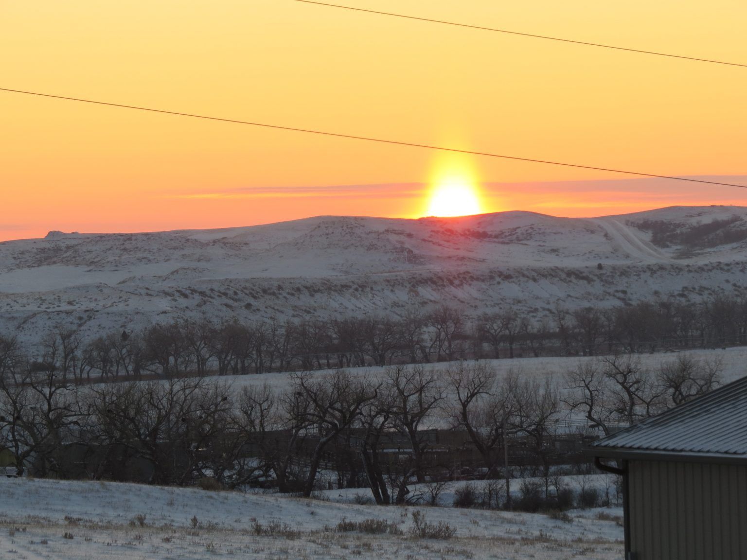 A sunset over a snowy landscape with a house in the foreground