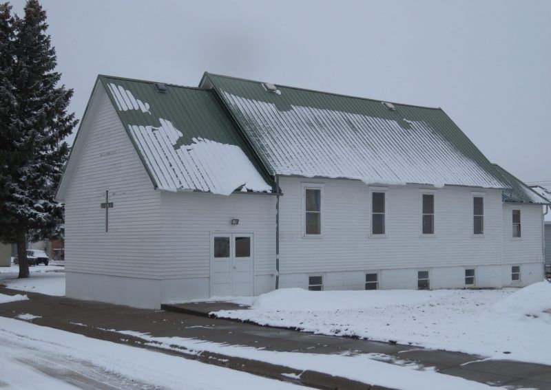 A white building with a green roof is covered in snow