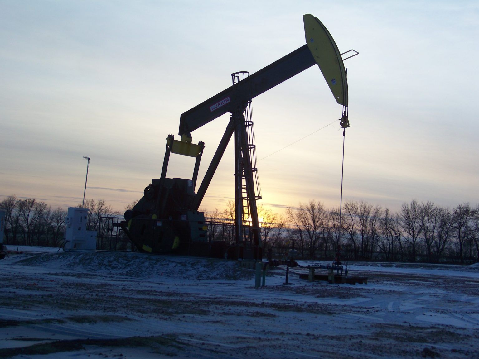 An oil pump in a snowy field at sunset