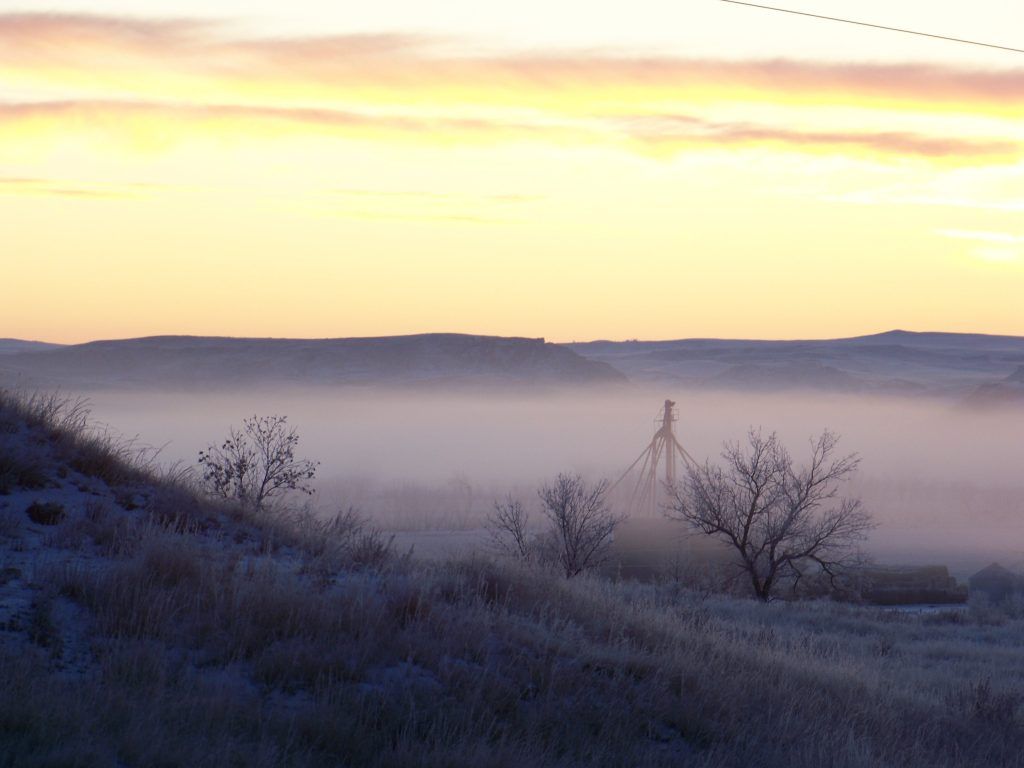 A foggy landscape with a sunset in the background