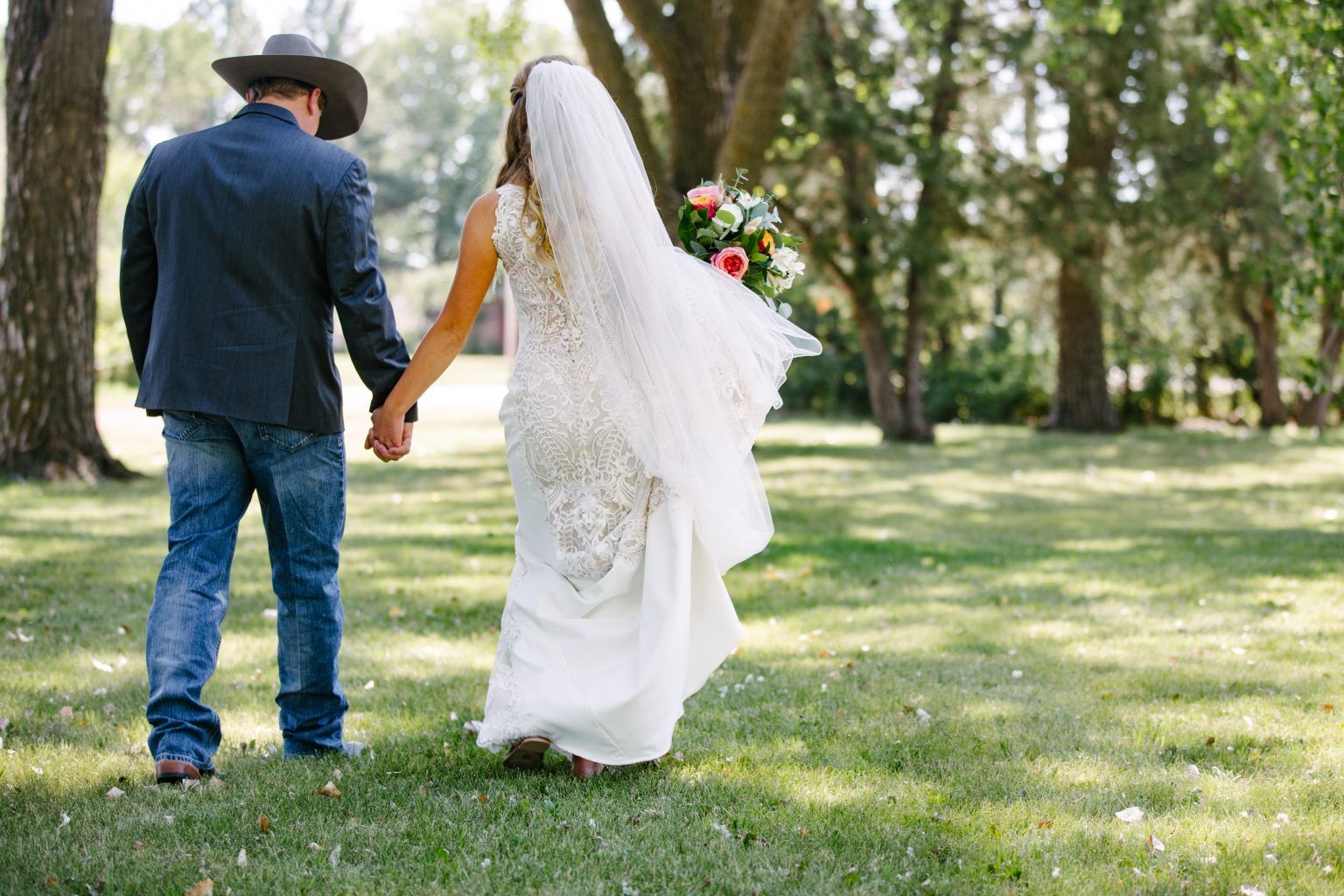 A bride and groom are holding hands while walking through a park.